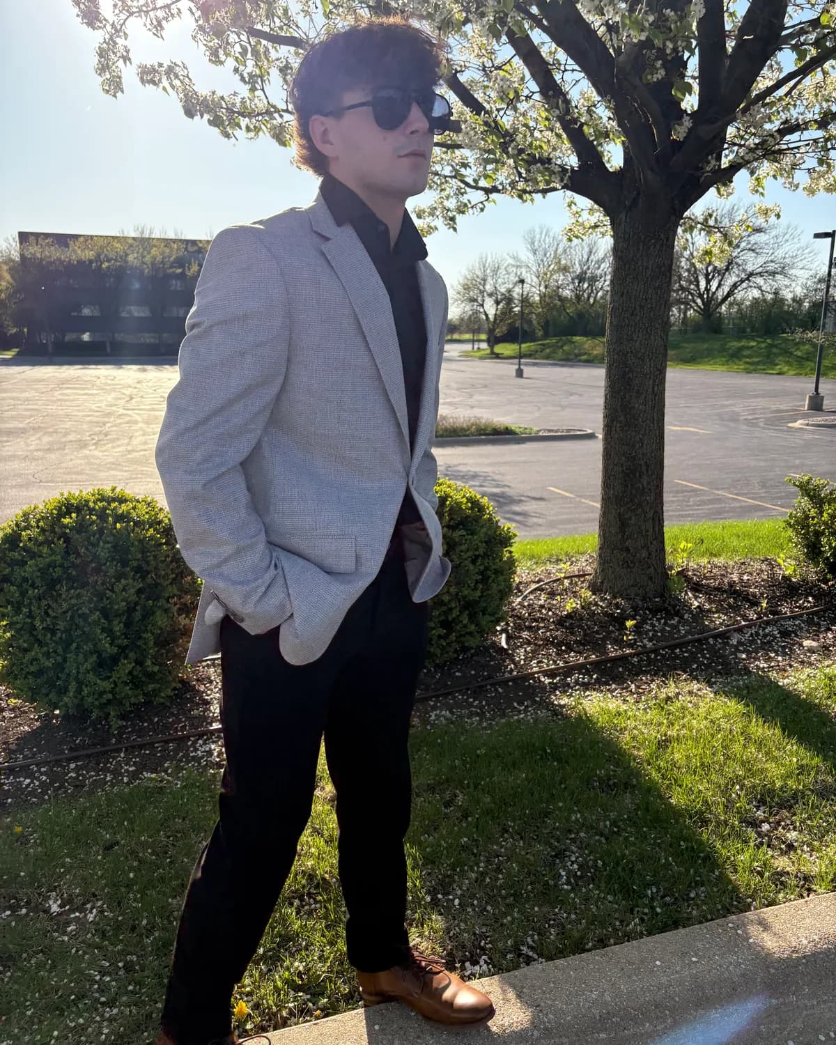 Noah Ciolkosz, founder of Ciolk OS, standing outside under a flowering tree in a light gray blazer, dark shirt and sunglasses.